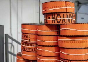 Canyon Rigging Winch Straps dispalyed in a triangular method. The winch straps are orange and rolled into a cylinder. They are held together with an elastic band.