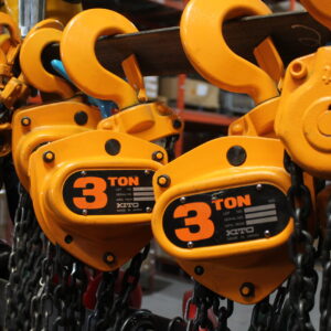 product photo of manual chain hoist. The chain hoist is a yellow orange colour with a big three on the side. The hoist is on a display wall and can be seen with other chain hoists of the same brand.